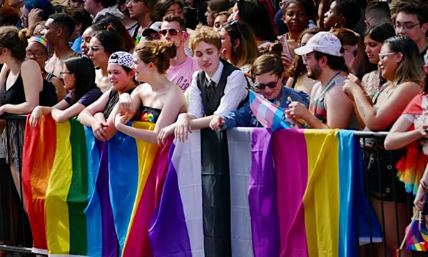 A crowd of people with various colorful striped flags draped over a fence